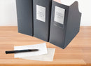 Three black binders with labels on a wooden surface, accompanied by a pen and paper.