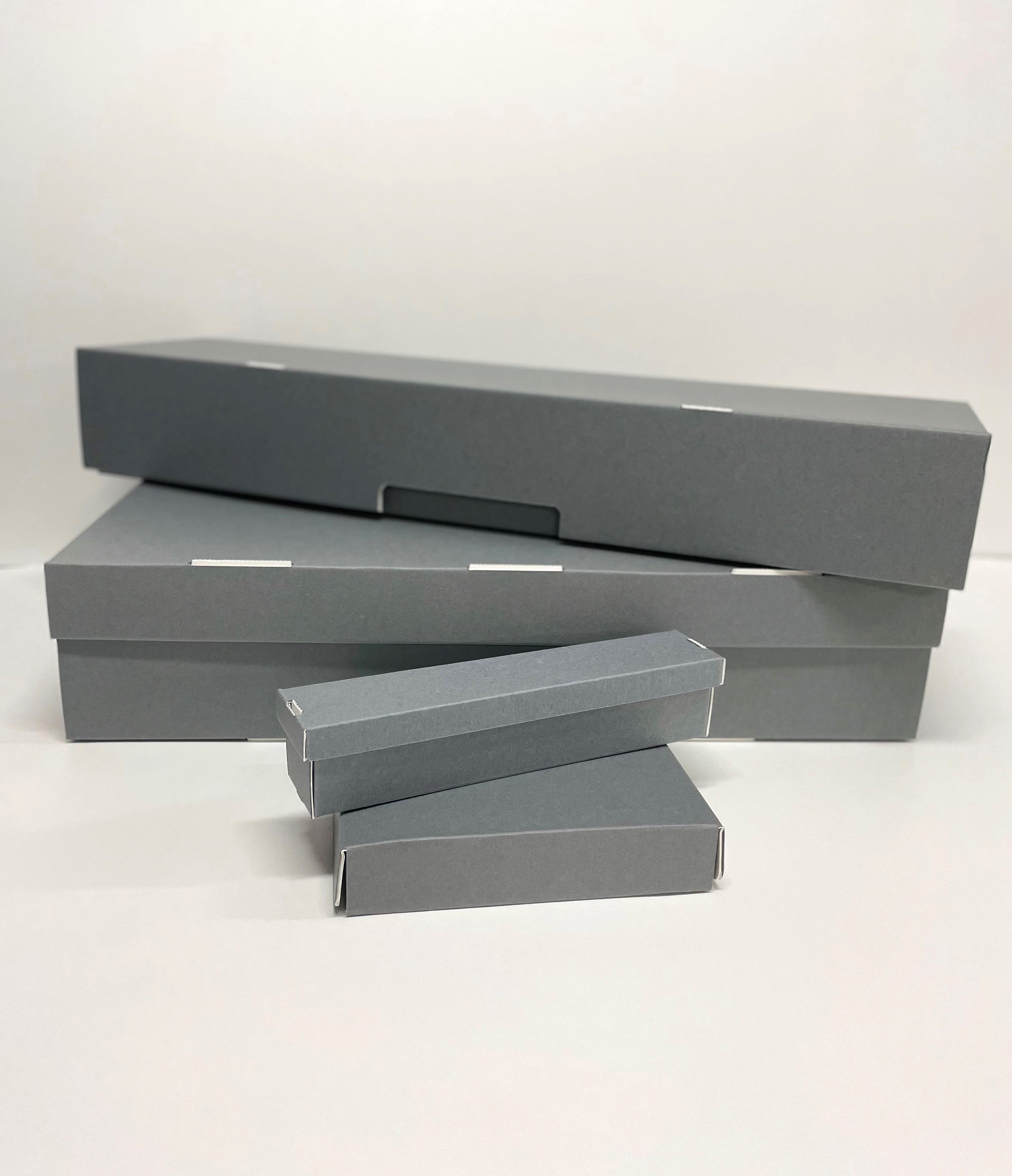 A set of gray custom-made boxes of various sizes, made from archival materials, displayed flat on a white surface.